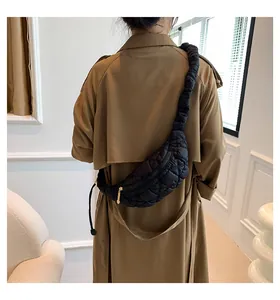 Stylish black quilted puffer crossbody chest bag worn over a classic brown trench coat.