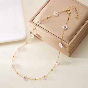 Dainty gold chain necklace featuring small pearl flowers and beads on a jewelry box.