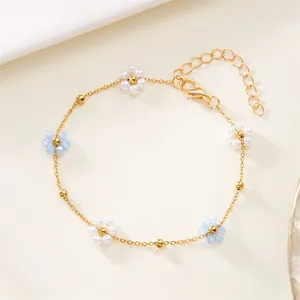 Detailed view of a gold chain bracelet featuring white pearl and blue beaded flower charms.