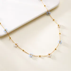 Close-up detail of a delicate gold chain with small blue and white pearl flowers