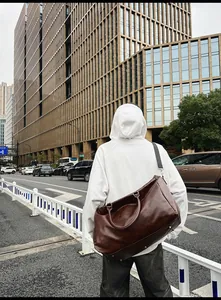 Man carrying a large brown vintage PU leather travel duffle bag on a busy city street.