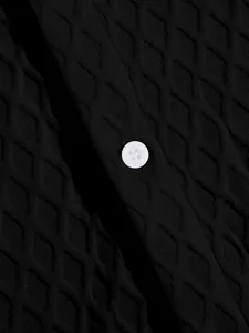 Close-up of black men's knit polo shirt with diamond jacquard pattern and white button.