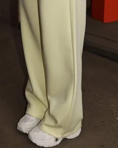 Detail of pale yellow wide-leg sweatpants hem paired with white chunky sneakers