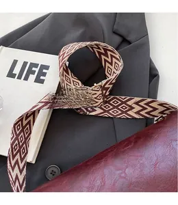 Detailed view of the geometric diamond patterned wide shoulder strap on a burgundy bag
