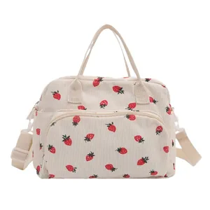 Cream corduroy travel bag with all-over red strawberry print and shoulder strap