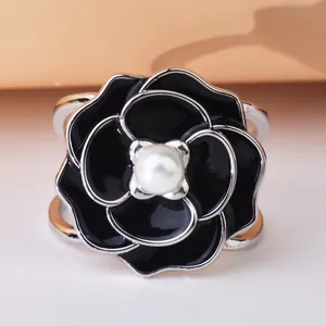 Detailed view of a black enamel camellia scarf buckle with a central white pearl