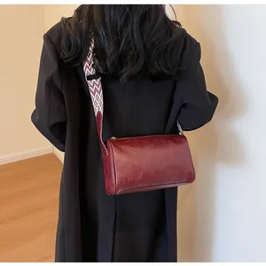 Burgundy faux leather pillow bag with patterned wide strap shown on a model's shoulder.