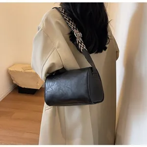 Elegant black leather cylinder bag with bohemian wide strap worn by a person in a coat