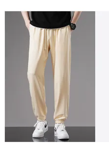 Detail shot of men's loose cream-colored cotton joggers with elastic cuffs.