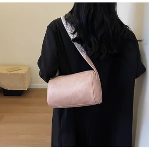 Stylish pink cylinder pillow bag with patterned wide strap shown on model's shoulder