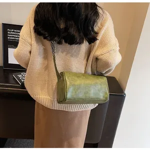 Stylish green leather cylinder crossbody pillow bag worn by a model in a cozy lifestyle setting