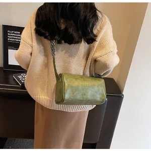 Close-up of olive green cylinder crossbody bag with patterned wide strap on shoulder