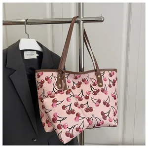 Détail montrant le grand sac cabas rose imprimé cerises et sa pochette sur un cintre