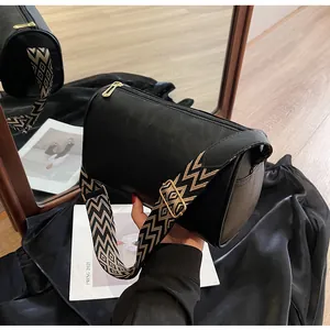 Detailed view of black barrel bag featuring a wide geometric pattern crossbody strap