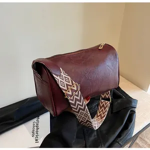 Close-up of deep burgundy barrel bag with vintage geometric patterned wide strap.