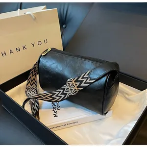 Detailed view of a black pillow bag with a geometric wide shoulder strap in a gift box