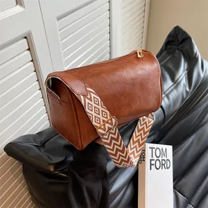 Fashionable brown leather pillow bag featuring a wide geometric woven shoulder strap