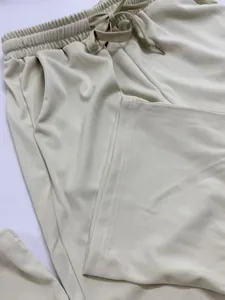Close-up detail of cream casual trousers showing drawstring waist and fabric texture.