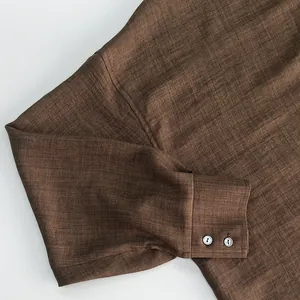Close-up detail showing the rich brown linen texture and buttoned cuff of this women's shirt