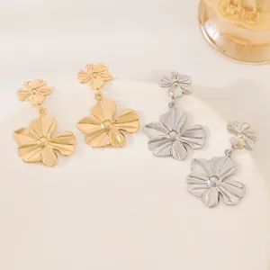 Close-up of minimalist golden and silver floral dangle earrings on a white plate.