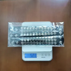 Macro view of two punk style heart rivet bracelets being weighed on a white digital scale.
