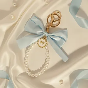 Elegant light blue bow keychain with white pearl loop and golden charm accessory detail.