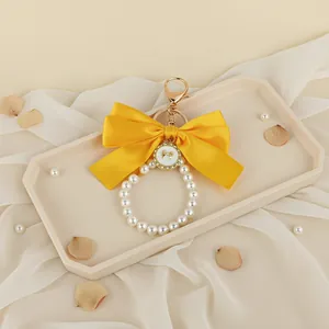 Detailed view of a large yellow satin bow keychain with a white pearl bead loop charm