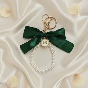 Close-up of an elegant dark green satin bow and pearl beaded keychain on silk background