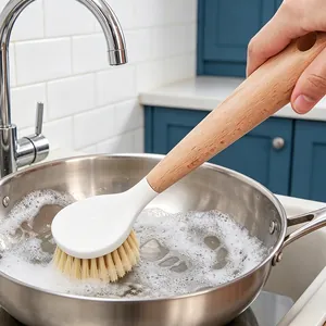 Sustainable wooden dish brush with long handle cleaning a soapy stainless steel pan