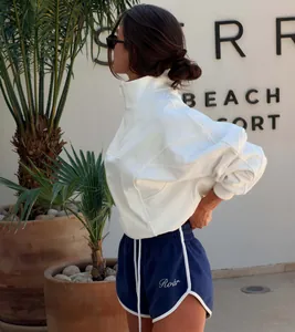 Woman wearing white half-zip sweatshirt and navy athletic shorts set in beach resort setting