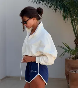 Model wearing a white half-zip cropped sweatshirt and navy blue gym shorts set outdoors