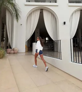 Model wearing a white half-zip sweatshirt and navy athletic shorts in a modern courtyard