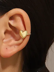 Close-up detail of golden heart-shaped ear cuff worn on model's ear cartilage