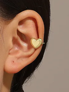 Close-up of a gold heart-shaped non-pierced ear cuff on a model's ear.