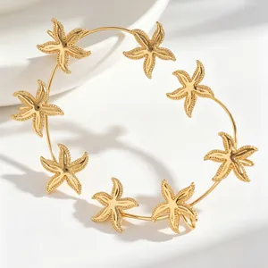 Dettaglio di un ear cuff dorato a forma di stella marina con ciondoli testurizzati.
