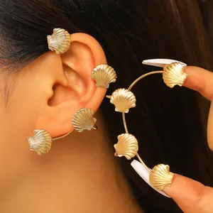 Dettaglio ravvicinato di un ear cuff dorato a forma di conchiglia su un orecchio di modella.