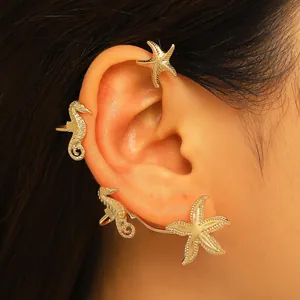 Primo piano di ear cuff dorati con motivi a stella marina e cavalluccio marino.
