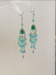 Detailansicht der silbernen Ohrringe im Ethno-Stil mit grünen Kristallen und blauen Perlenquasten.