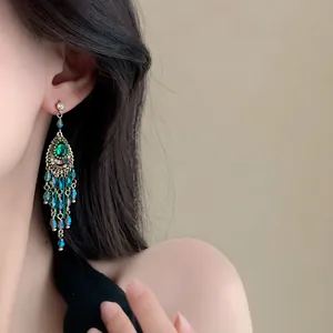 Detailaufnahme von Boho-Quastenohrringen mit grünen Kristallen an einem asiatischen Model