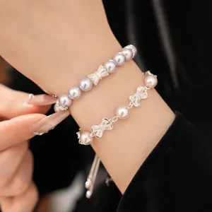 Detail of two layered pearl bracelets with sparkling bow-shaped zircon charms