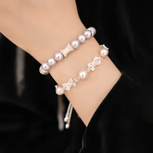 Close-up detail of elegant pearl bracelets featuring sparkling zircon bow charms on a wrist.