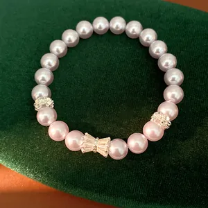 Close-up view of light purple pearl bracelet with zircon bow and floral charms on green velvet.