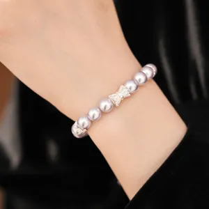Detail shot of a light purple pearl bracelet with a sparkling zircon bow charm on a wrist.
