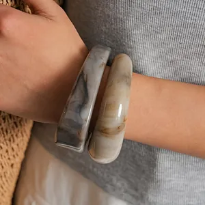 Gros plan de bracelets joncs en résine marbrée portés au poignet pour un look chic.