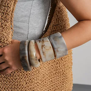 Gros plan de bracelets en résine marbrée portés avec un gilet en paille