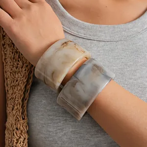 Gros plan de joncs ouverts en résine marbrée au style minimaliste portés par une femme