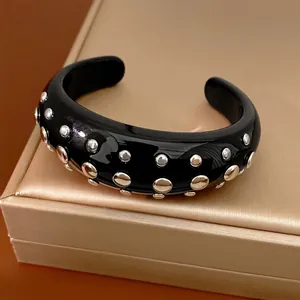 Stoere zwarte hars open armband met ronde metalen klinknagels op een gouden display