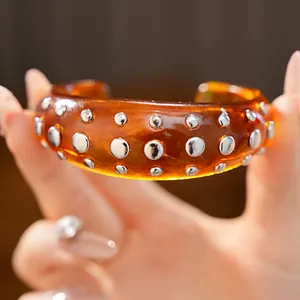 Close-up van een barnsteenkleurige hars armband met glanzende zilveren studs