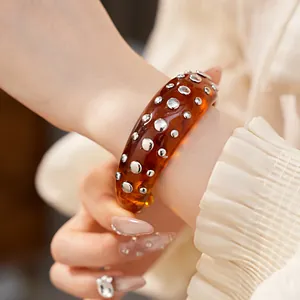 Detailopname van een amberkleurige hars armband met zilveren klinknagels op de pols