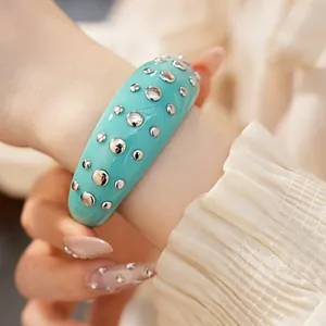 Close-up van een grove turquoise hars armband versierd met zilveren metalen klinknagels.
